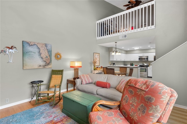 living room featuring ceiling fan with notable chandelier, a high ceiling, and light hardwood / wood-style flooring