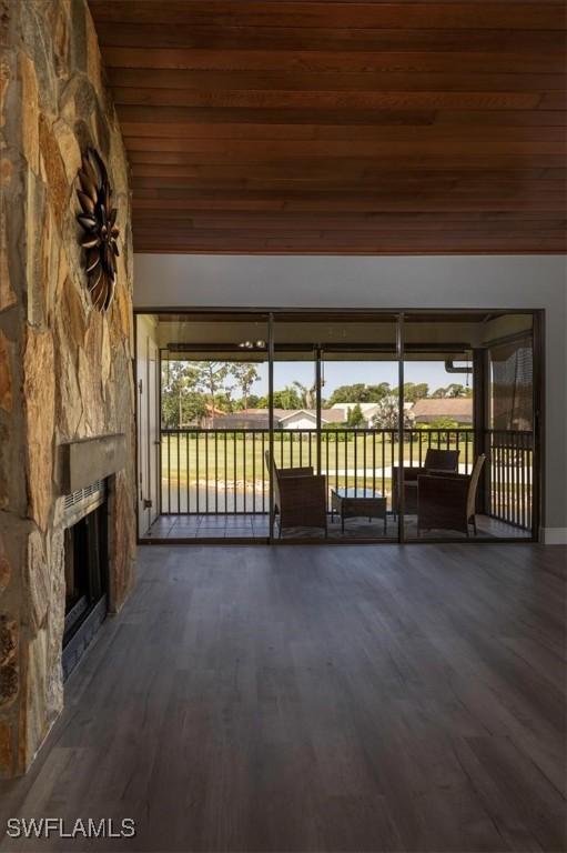 unfurnished living room featuring dark wood-type flooring, wooden ceiling, a stone fireplace, and vaulted ceiling