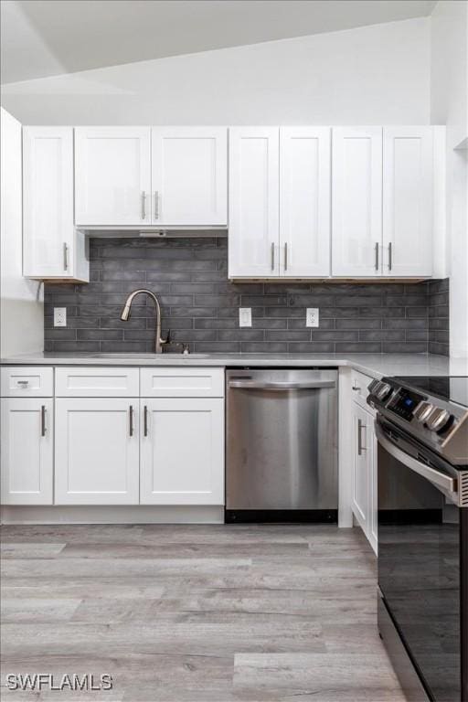 kitchen featuring vaulted ceiling, appliances with stainless steel finishes, light hardwood / wood-style flooring, and white cabinetry