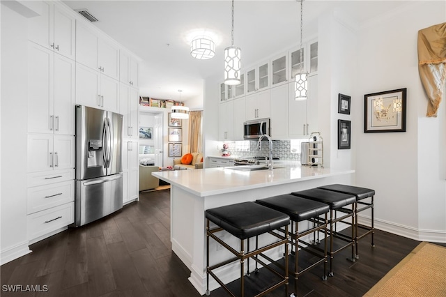 kitchen featuring kitchen peninsula, white cabinets, decorative light fixtures, and appliances with stainless steel finishes