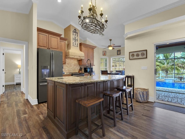 kitchen with stainless steel fridge, dark wood-type flooring, a center island with sink, decorative backsplash, and lofted ceiling