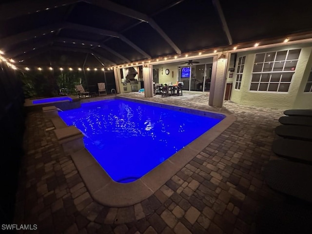 pool at night with glass enclosure, ceiling fan, and a patio