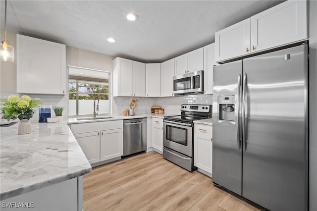 kitchen with decorative light fixtures, sink, stainless steel appliances, white cabinets, and light stone counters