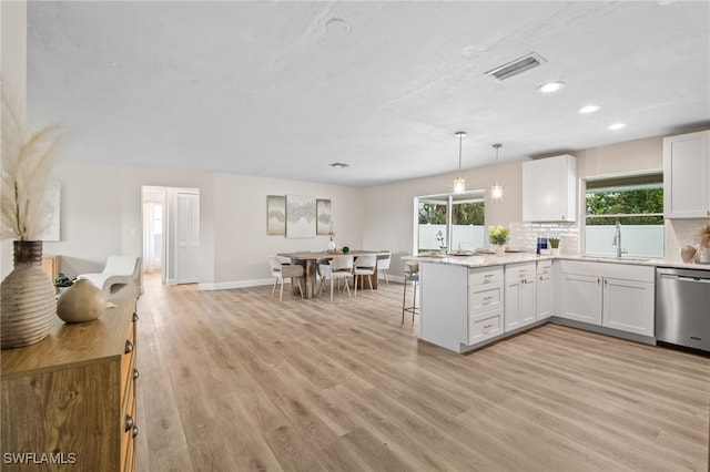 kitchen featuring kitchen peninsula, stainless steel dishwasher, white cabinets, and hanging light fixtures