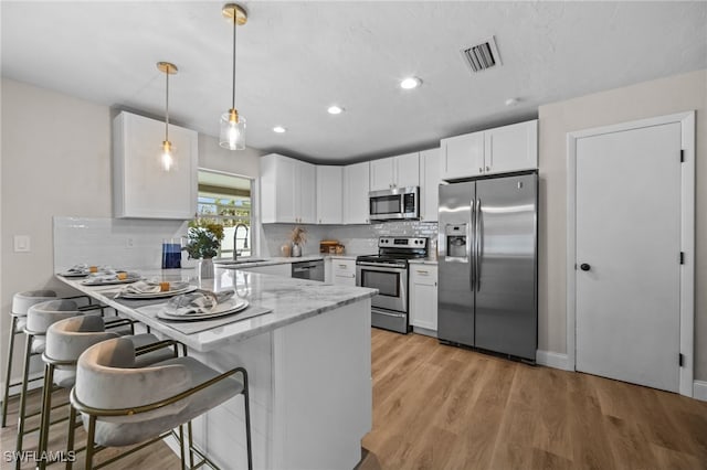 kitchen with white cabinets, appliances with stainless steel finishes, decorative light fixtures, a kitchen bar, and kitchen peninsula