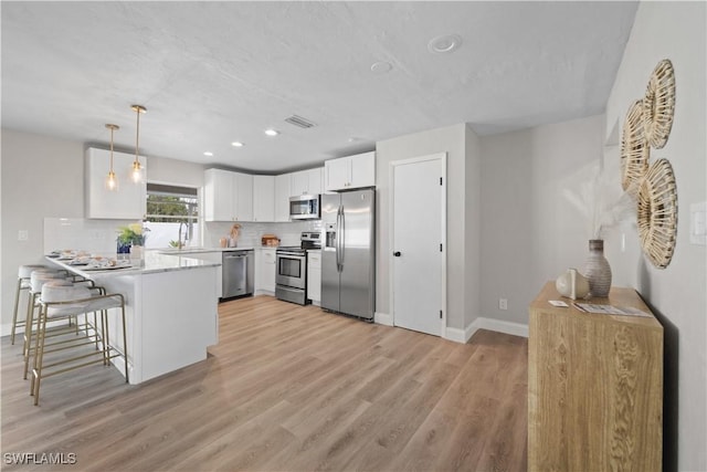 kitchen with white cabinetry, kitchen peninsula, stainless steel appliances, pendant lighting, and a breakfast bar