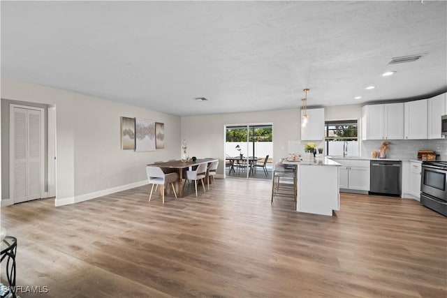 kitchen featuring decorative light fixtures, a kitchen island, hardwood / wood-style flooring, appliances with stainless steel finishes, and white cabinets