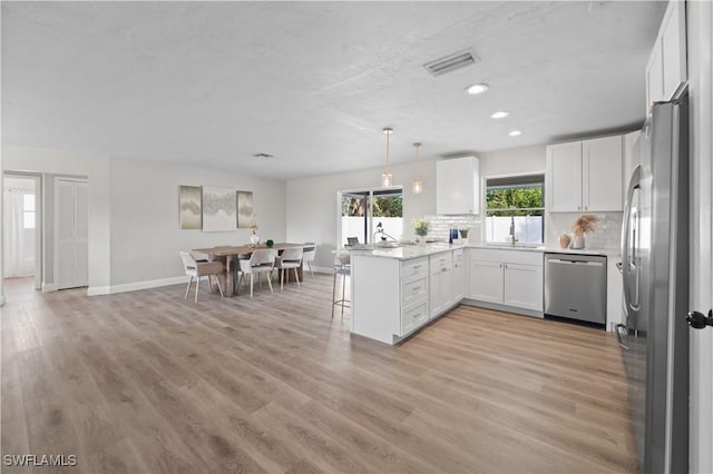 kitchen with decorative backsplash, kitchen peninsula, white cabinetry, hanging light fixtures, and stainless steel appliances