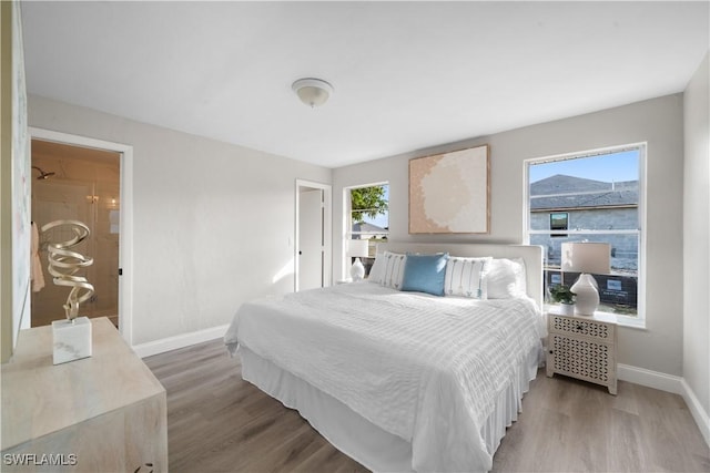 bedroom with connected bathroom, hardwood / wood-style flooring, and multiple windows