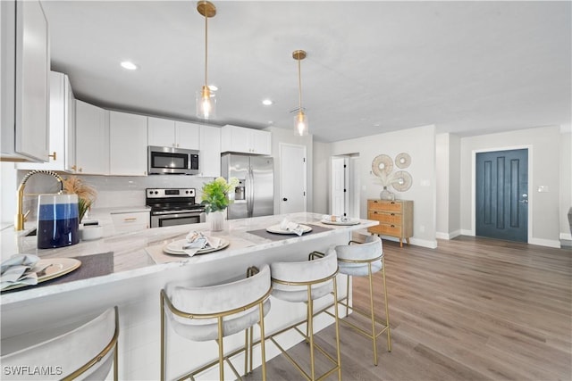 kitchen featuring white cabinetry, hardwood / wood-style floors, a breakfast bar area, stainless steel appliances, and pendant lighting