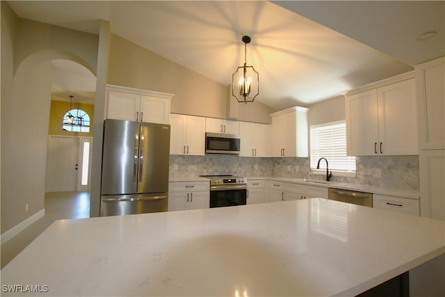 kitchen featuring pendant lighting, vaulted ceiling, decorative backsplash, white cabinets, and appliances with stainless steel finishes