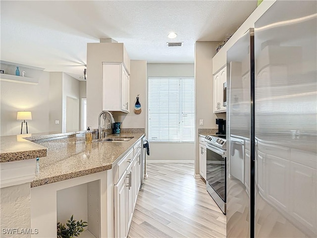 kitchen featuring a textured ceiling, stainless steel appliances, sink, light hardwood / wood-style flooring, and white cabinetry