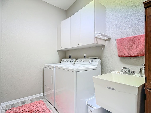 laundry room featuring washing machine and clothes dryer, sink, cabinets, and light hardwood / wood-style flooring