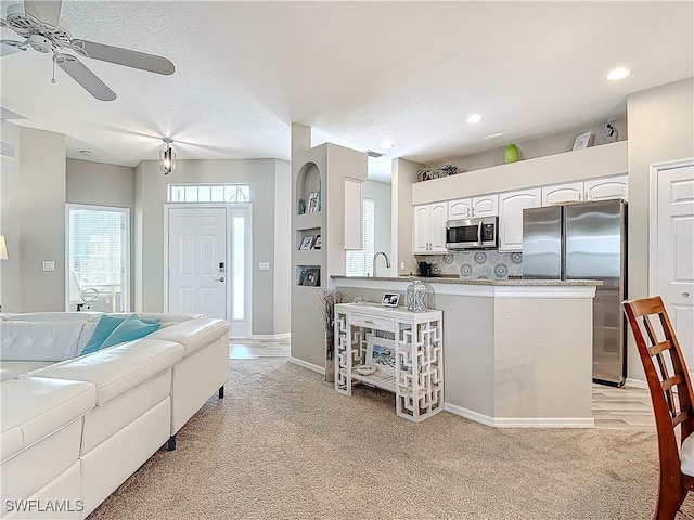 kitchen featuring backsplash, ceiling fan, light colored carpet, white cabinetry, and stainless steel appliances