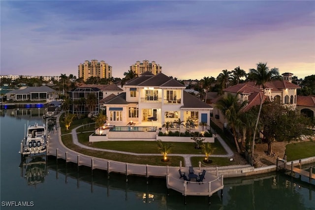 back house at dusk featuring a balcony, a patio, a lawn, and a water view