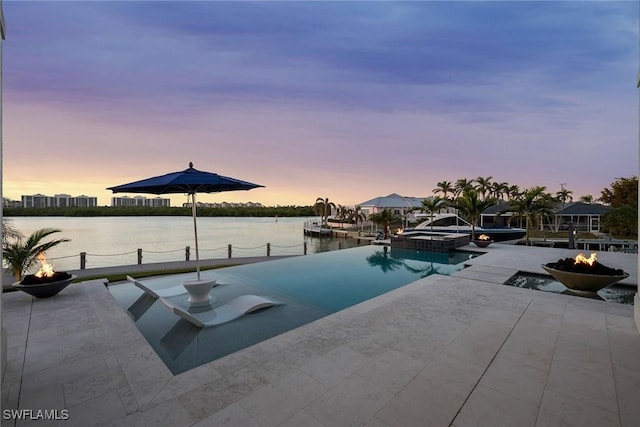 pool at dusk with a patio, a fire pit, and a water view