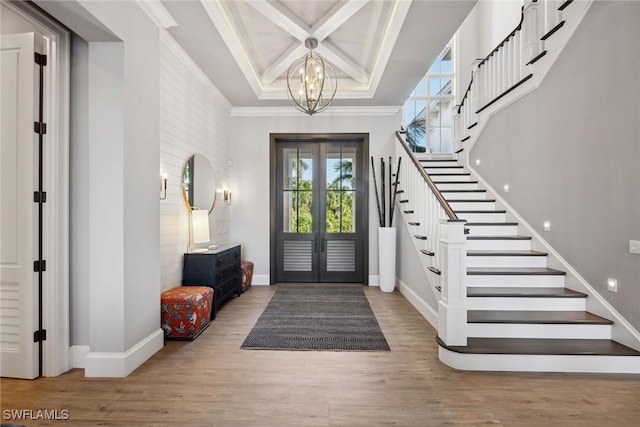 foyer entrance with french doors, wood-type flooring, ornamental molding, and a chandelier