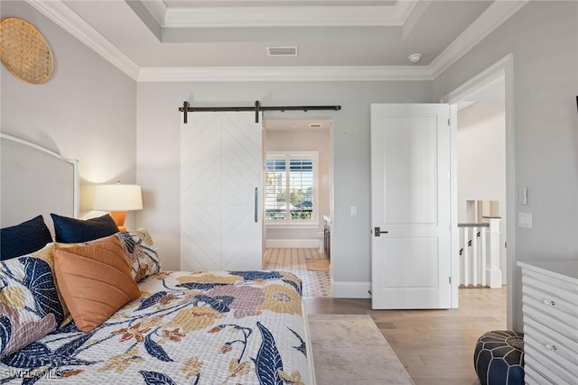 bedroom featuring ornamental molding, light wood-type flooring, a raised ceiling, and a barn door