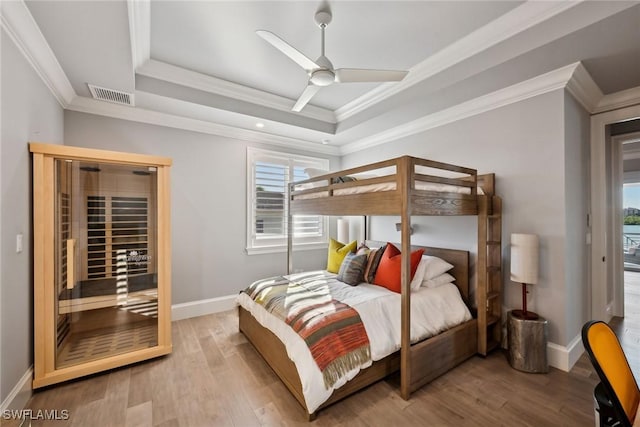 bedroom featuring ornamental molding, light wood-type flooring, ceiling fan, and a tray ceiling