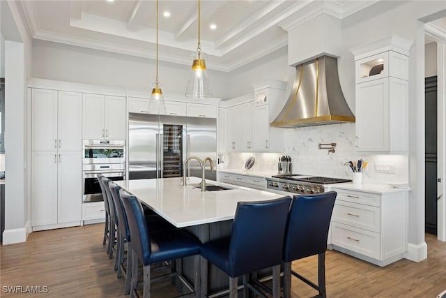 kitchen with white cabinets, decorative backsplash, a center island with sink, wall chimney range hood, and appliances with stainless steel finishes