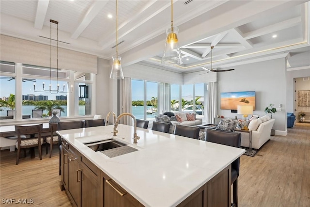 kitchen with pendant lighting, an island with sink, light wood-type flooring, beamed ceiling, and sink