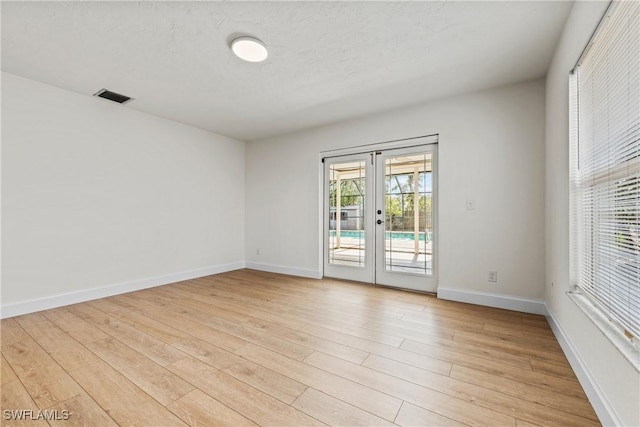 spare room featuring french doors, a textured ceiling, and light wood-type flooring