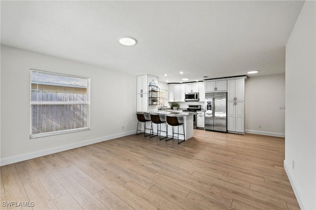 kitchen featuring white cabinetry, light wood-type flooring, appliances with stainless steel finishes, a kitchen breakfast bar, and kitchen peninsula