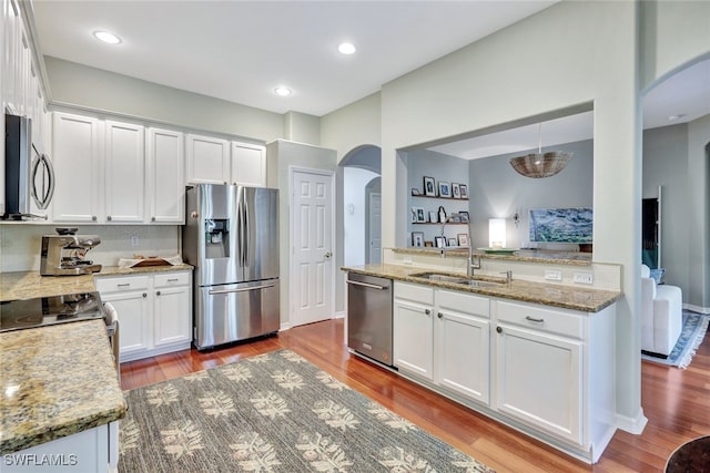 kitchen with sink, appliances with stainless steel finishes, pendant lighting, white cabinets, and light wood-type flooring