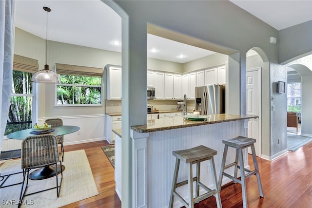 kitchen with appliances with stainless steel finishes, stone countertops, white cabinetry, and light hardwood / wood-style floors