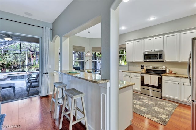 kitchen featuring light stone countertops, appliances with stainless steel finishes, pendant lighting, light hardwood / wood-style floors, and white cabinetry