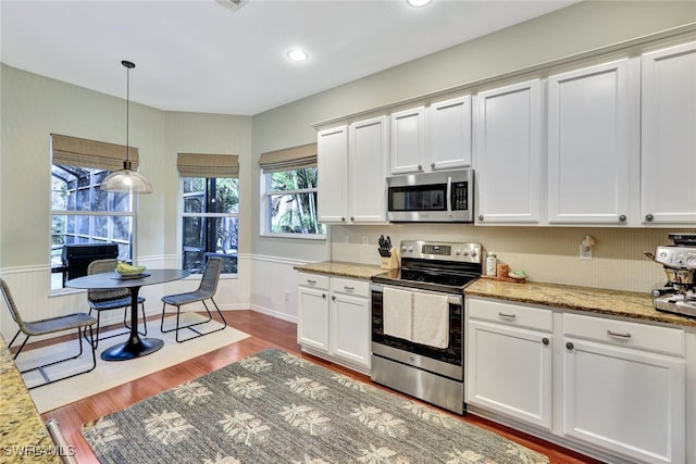 kitchen with white cabinetry, stainless steel appliances, light stone counters, hardwood / wood-style floors, and pendant lighting