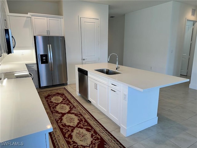 kitchen with a kitchen island with sink, sink, light tile patterned floors, appliances with stainless steel finishes, and white cabinetry