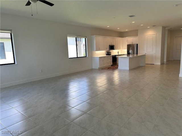 interior space with light tile patterned floors, stainless steel appliances, white cabinetry, and an island with sink