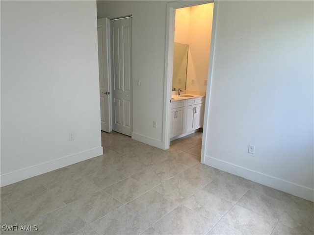 unfurnished bedroom featuring light tile patterned flooring, ensuite bathroom, a closet, and sink