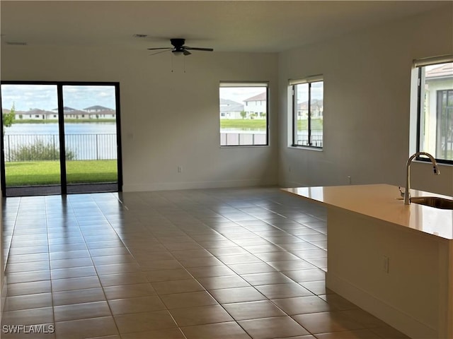 tiled spare room featuring ceiling fan, a water view, and sink