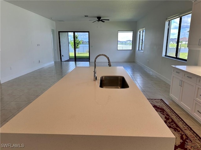 kitchen featuring ceiling fan, sink, light tile patterned floors, a center island with sink, and white cabinets