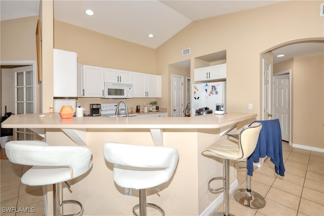 kitchen with kitchen peninsula, white appliances, a breakfast bar area, and white cabinetry