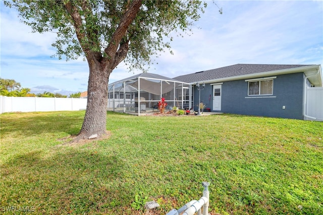 rear view of property featuring glass enclosure and a yard