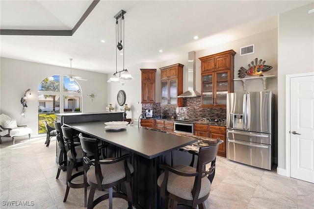 kitchen with pendant lighting, a kitchen breakfast bar, wall chimney range hood, decorative backsplash, and stainless steel appliances