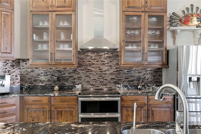 kitchen with backsplash, stainless steel appliances, dark stone counters, and wall chimney exhaust hood