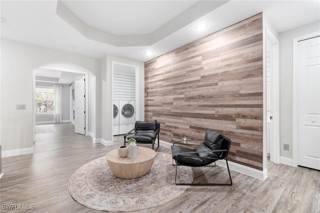 sitting room featuring a tray ceiling, washing machine and clothes dryer, light wood-type flooring, and wooden walls