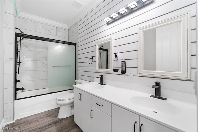 full bathroom featuring toilet, vanity, wood-type flooring, enclosed tub / shower combo, and ornamental molding