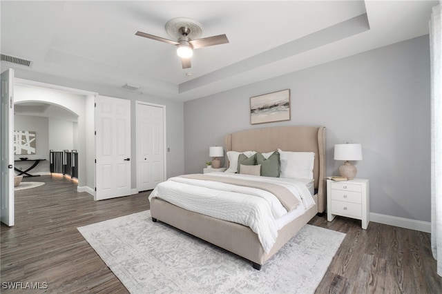 bedroom with ceiling fan, a tray ceiling, and dark hardwood / wood-style flooring