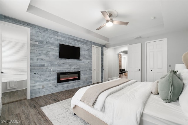 bedroom with ceiling fan, dark hardwood / wood-style floors, a tray ceiling, and two closets