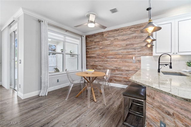 dining room with dark hardwood / wood-style flooring, wooden walls, sink, ceiling fan, and crown molding