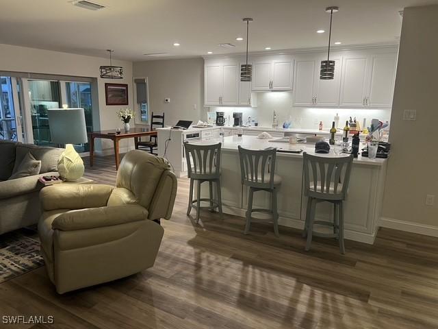 kitchen featuring white cabinets, a kitchen breakfast bar, dark hardwood / wood-style flooring, and hanging light fixtures