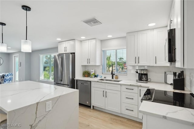 kitchen featuring white cabinets, sink, hanging light fixtures, appliances with stainless steel finishes, and light stone counters