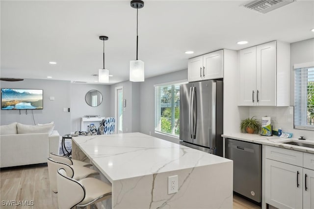 kitchen with a center island, hanging light fixtures, light stone counters, white cabinets, and appliances with stainless steel finishes