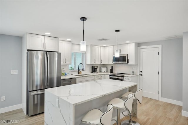 kitchen with appliances with stainless steel finishes, sink, pendant lighting, a center island, and white cabinetry