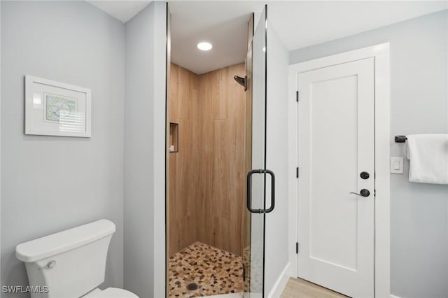 bathroom featuring a shower with door and toilet